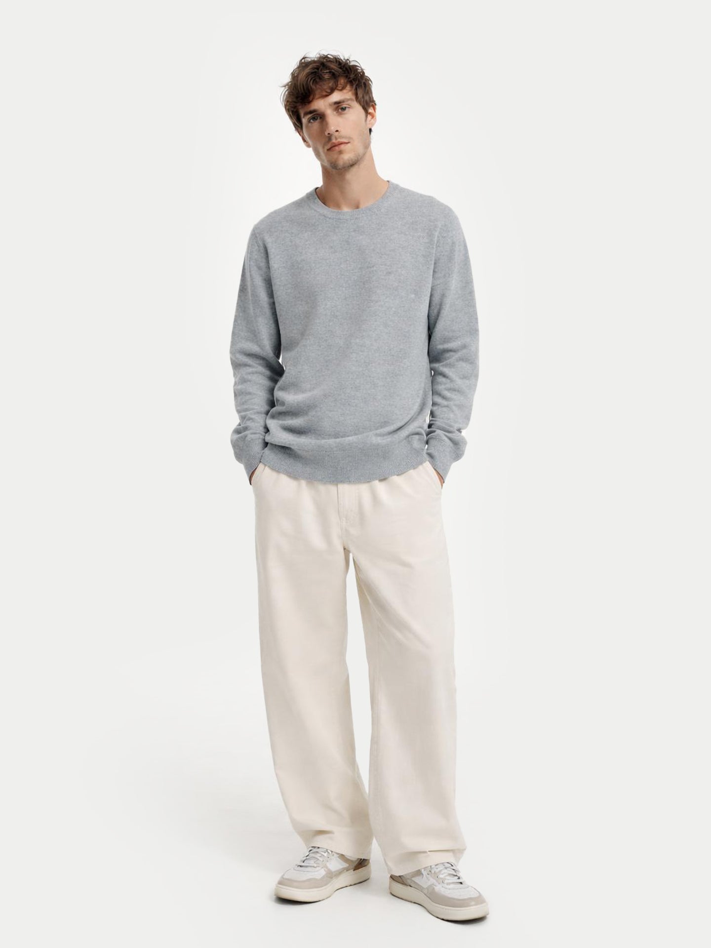 Man wearing a gray sweater and white pants on a white background