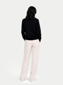 Person wearing a black sweater and light pink pants on a white background