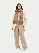 Person wearing a beige scarf, coat, and pants on a white background