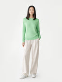 Person wearing a green sweater and white pants on a light gray background #color_green-ash