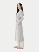 side view of a woman wearing a long light gray coat on a white background. #color_steel-silver #ai-image