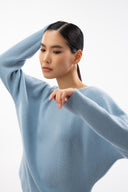 A woman in a pale blue seamless cashmere sweater, one arm raised, against a white background