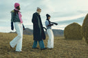 Three people in cashmere coats and knitwear walking across the steppe past hay bales