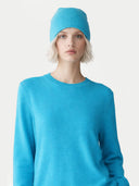 Person wearing a blue sweater and matching winter hat against a white background #color_peacock-blue