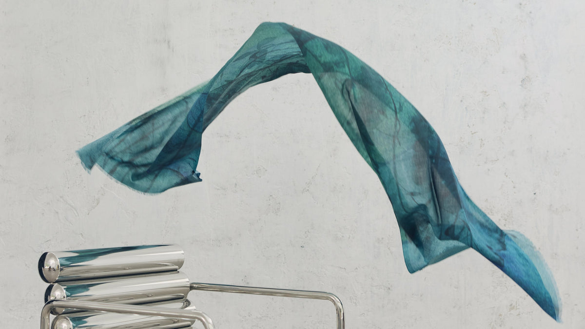 Teal cashmere scarf caught mid-air against a concrete wall