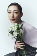 A woman in a lilac cashmere cardigan holding white flowers, studio portrait