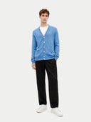 Man wearing a blue cardigan, white shirt, black pants, and white sneakers on a light gray background. #color_blue #ai-image