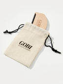 A beige cashmere comb with a light camel handle, placed inside a beige fabric pouch with the brand name 'GOBI' printed on it.